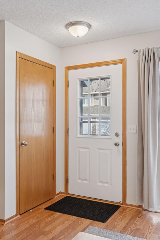 doorway to outside featuring a textured ceiling, baseboards, and light wood-style floors