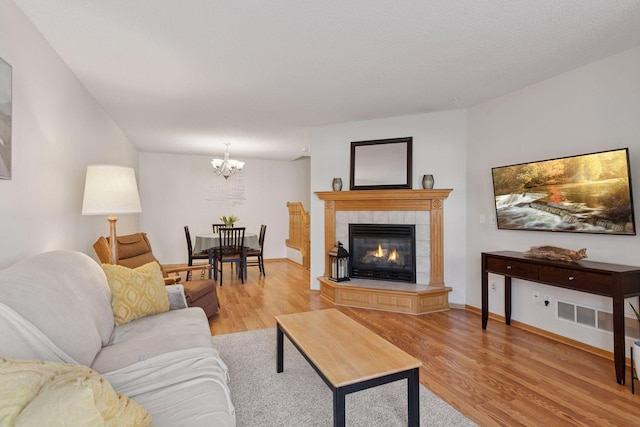 living area featuring baseboards, light wood-style flooring, a tiled fireplace, and an inviting chandelier