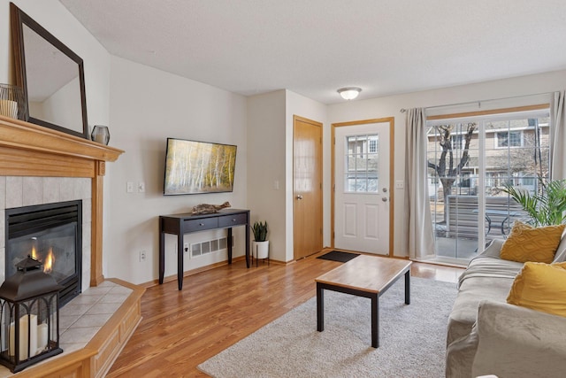 living area with baseboards, a fireplace, a textured ceiling, and light wood finished floors