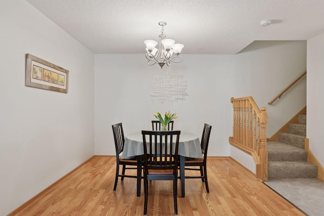 dining space with light wood-type flooring, a notable chandelier, a textured ceiling, and stairs