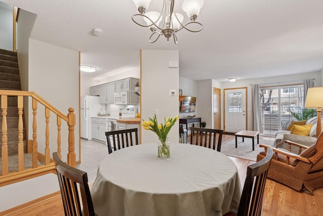 dining area with a textured ceiling, light wood-style flooring, an inviting chandelier, and stairs