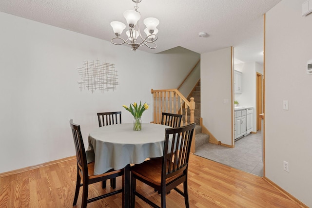 dining space featuring light wood-type flooring, stairs, a chandelier, and a textured ceiling