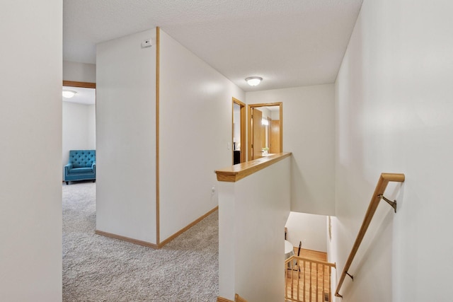 hallway featuring a textured ceiling, carpet flooring, an upstairs landing, and baseboards