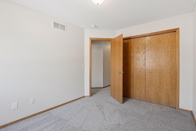 unfurnished bedroom featuring light carpet, baseboards, visible vents, a textured ceiling, and a closet