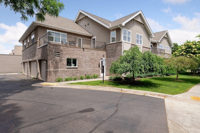 view of front facade featuring driveway, a balcony, an attached garage, a front lawn, and brick siding