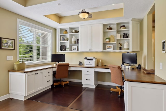 office area with dark wood-style flooring, visible vents, baseboards, built in study area, and a raised ceiling