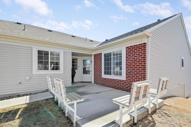 rear view of property featuring brick siding and roof with shingles