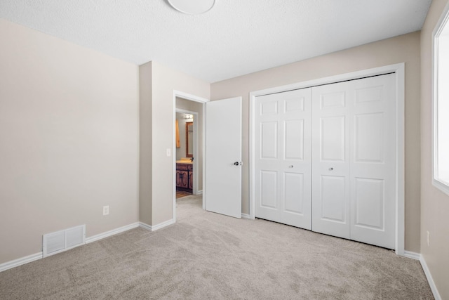 unfurnished bedroom with light carpet, a closet, and a textured ceiling