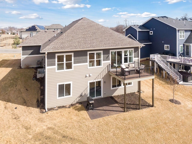 rear view of house with a shingled roof, a yard, a wooden deck, and a patio