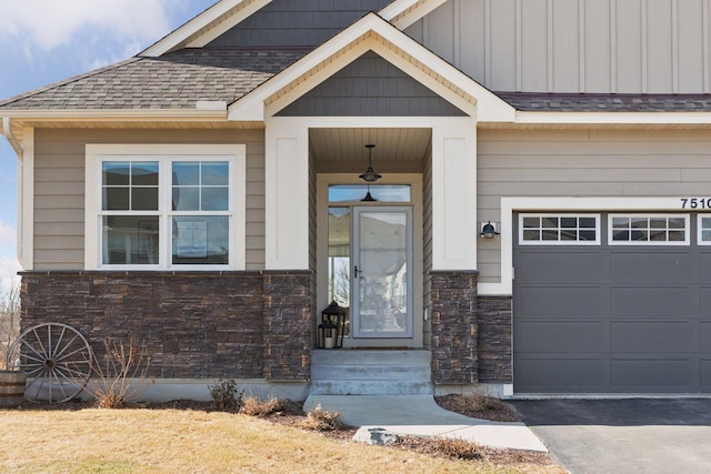 entrance to property featuring a garage, stone siding, and a shingled roof