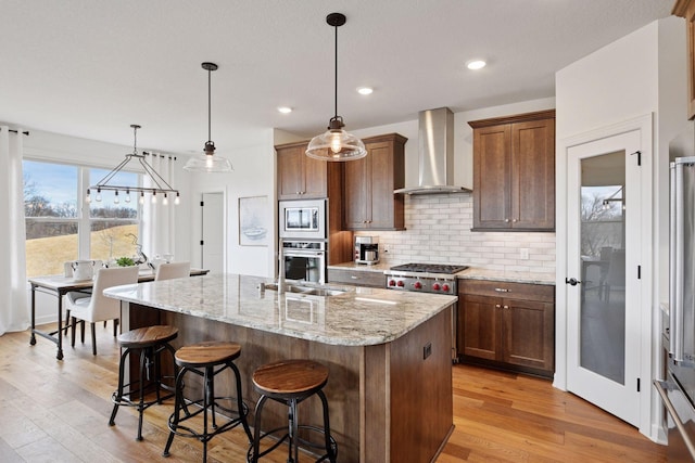 kitchen with light wood-type flooring, wall chimney exhaust hood, appliances with stainless steel finishes, and decorative backsplash