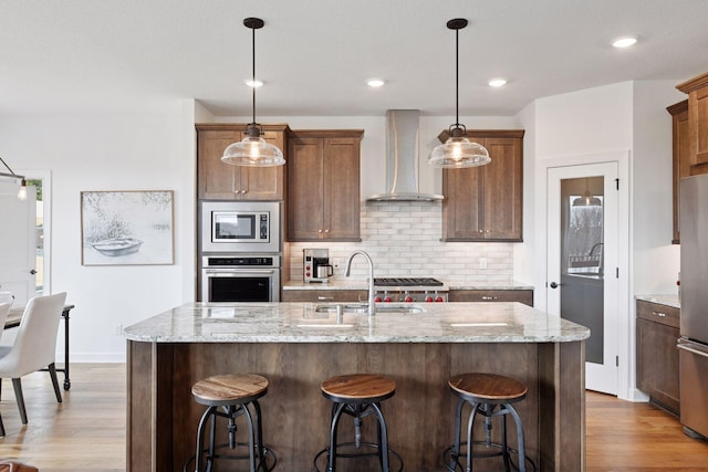 kitchen with wood finished floors, stainless steel appliances, wall chimney range hood, and a sink