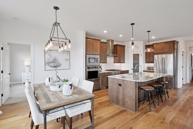 kitchen featuring decorative backsplash, an island with sink, wall chimney exhaust hood, stainless steel appliances, and a sink