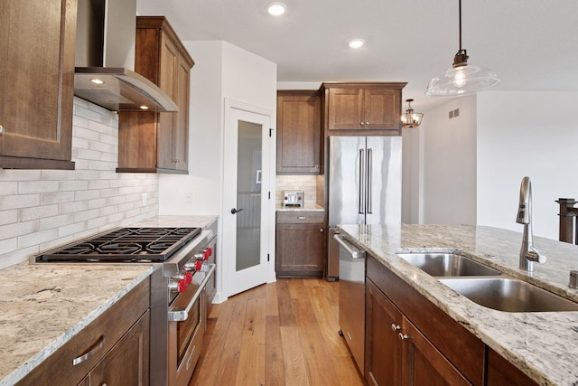 kitchen featuring premium appliances, wall chimney exhaust hood, light wood-type flooring, pendant lighting, and a sink