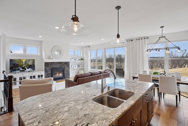 kitchen featuring wood-type flooring, a sink, a stone fireplace, and hanging light fixtures