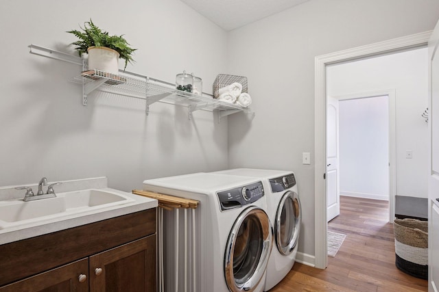 laundry area featuring light wood finished floors, a sink, separate washer and dryer, laundry area, and baseboards