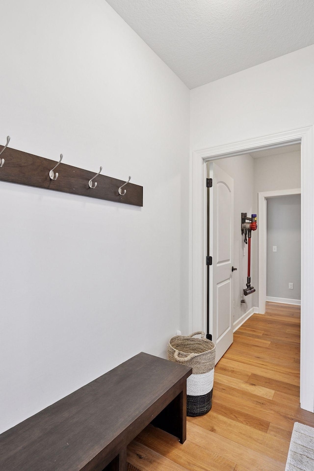 mudroom with light wood-style floors, a textured ceiling, and baseboards