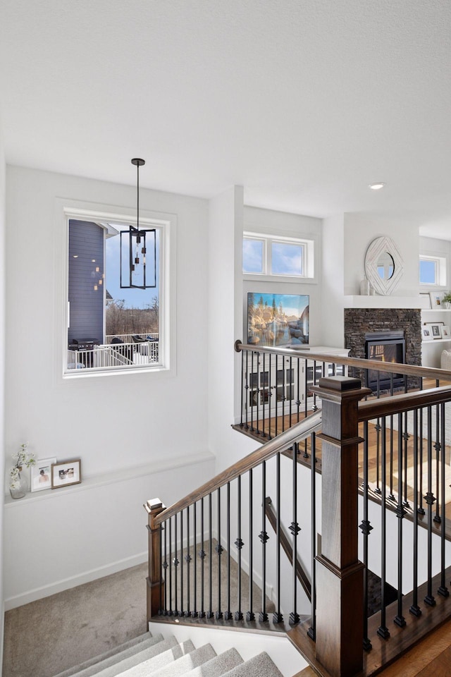 staircase featuring a chandelier, a stone fireplace, carpet, and baseboards