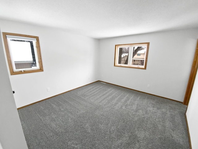 spare room featuring dark colored carpet and baseboards