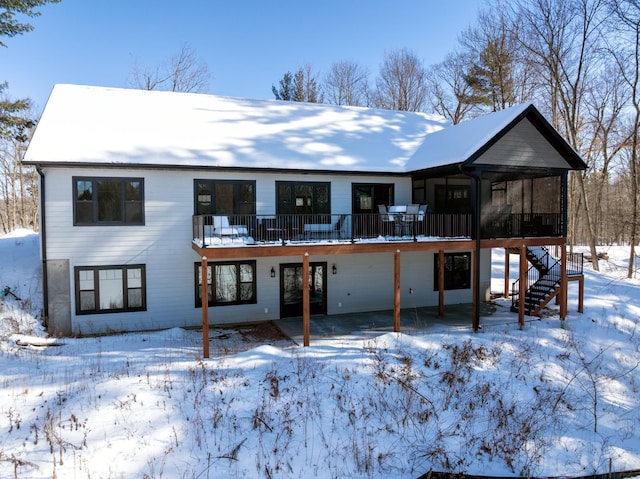 snow covered rear of property with stairs and a sunroom