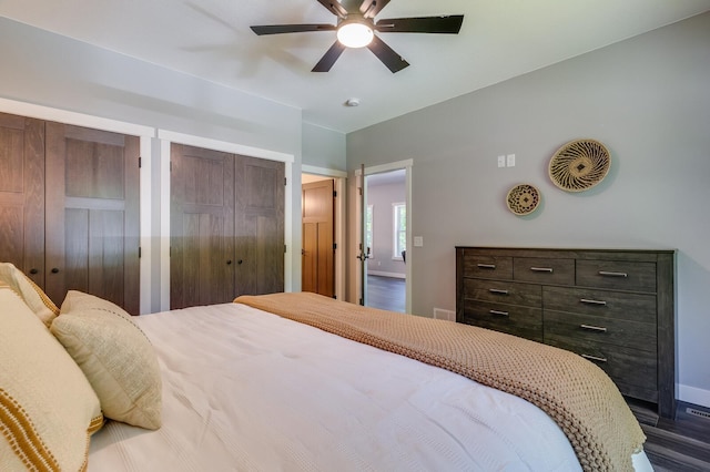 bedroom featuring ceiling fan, dark wood-type flooring, visible vents, baseboards, and two closets