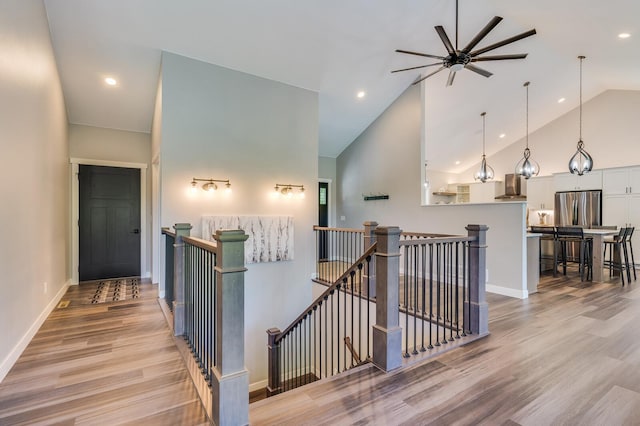 hall featuring recessed lighting, light wood-style floors, an upstairs landing, high vaulted ceiling, and baseboards