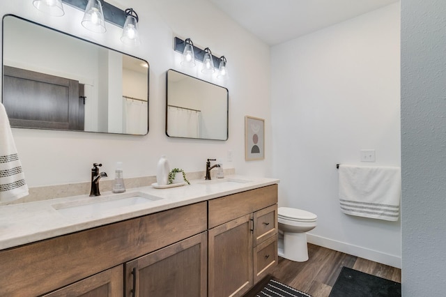 bathroom with double vanity, toilet, a sink, and wood finished floors