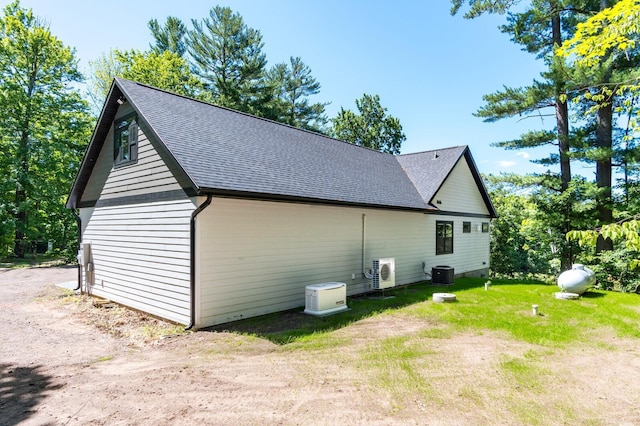 view of side of home with a shingled roof, ac unit, a yard, and central air condition unit