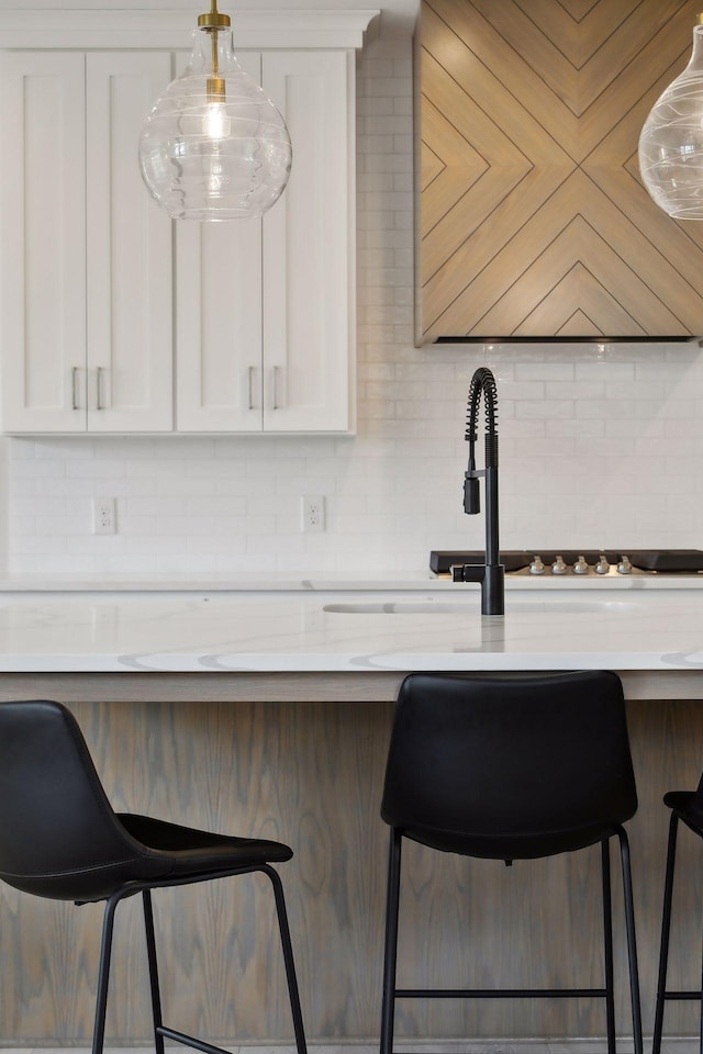 kitchen featuring white cabinetry, a breakfast bar, light stone counters, and decorative backsplash