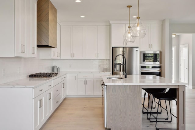 kitchen with hanging light fixtures, white cabinetry, appliances with stainless steel finishes, and a center island with sink