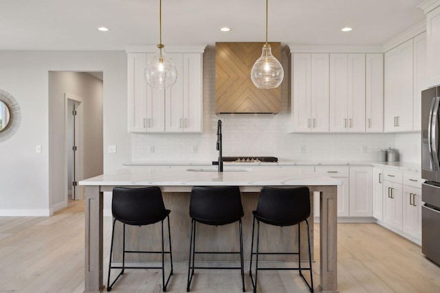 kitchen featuring light wood finished floors, a kitchen bar, stainless steel fridge, white cabinetry, and a sink