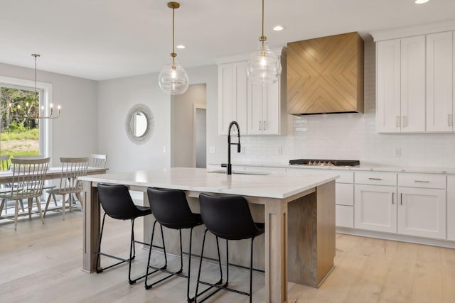 kitchen featuring custom range hood, a center island with sink, light wood finished floors, and a sink