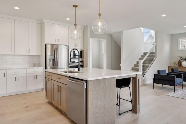 kitchen featuring tasteful backsplash, a sink, light stone counters, appliances with stainless steel finishes, and a kitchen island with sink