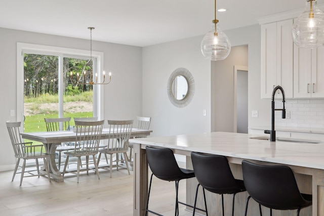 kitchen featuring light wood-type flooring, a sink, tasteful backsplash, white cabinets, and light stone countertops