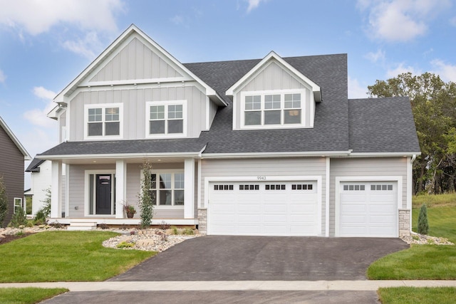 view of front facade featuring a front lawn, aphalt driveway, roof with shingles, covered porch, and an attached garage