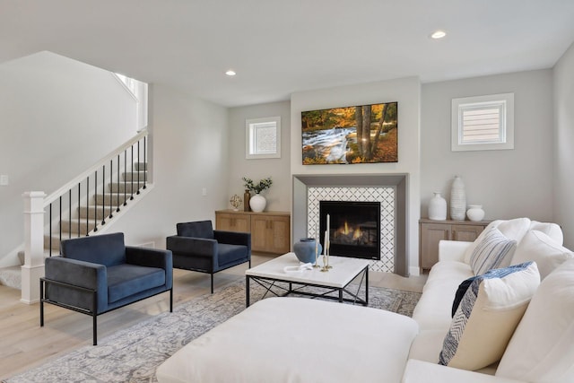 living area with a tiled fireplace, stairway, recessed lighting, and light wood-style flooring