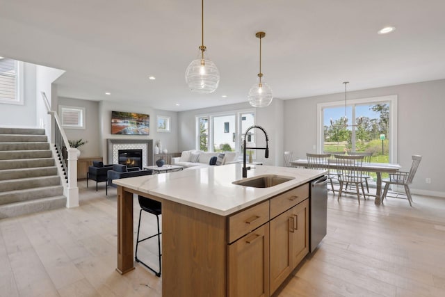 kitchen with a sink, light wood-style floors, a fireplace, light countertops, and dishwasher