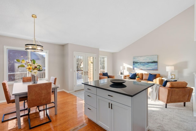 kitchen featuring vaulted ceiling, a kitchen island, hanging light fixtures, light hardwood / wood-style floors, and french doors