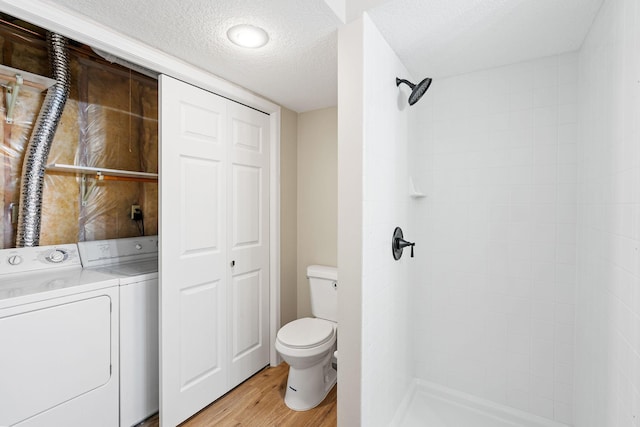 bathroom with hardwood / wood-style floors, independent washer and dryer, tiled shower, a textured ceiling, and toilet