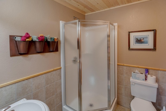 full bathroom featuring toilet, a wainscoted wall, wood ceiling, tile walls, and a stall shower