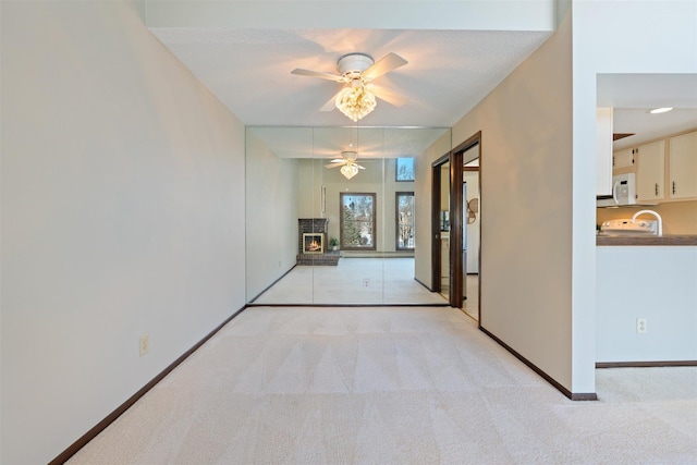 interior space with a brick fireplace, light carpet, and ceiling fan