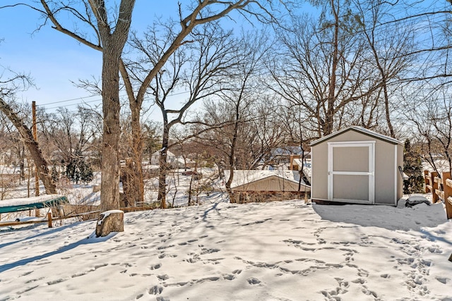 yard layered in snow featuring a storage unit, an outdoor structure, and fence