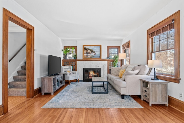 living room with stairway, a fireplace, light wood-style flooring, and a healthy amount of sunlight