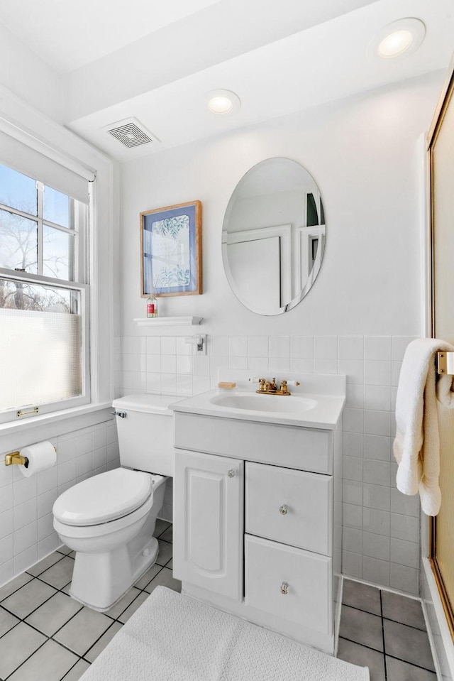 bathroom with visible vents, toilet, tile patterned floors, vanity, and tile walls