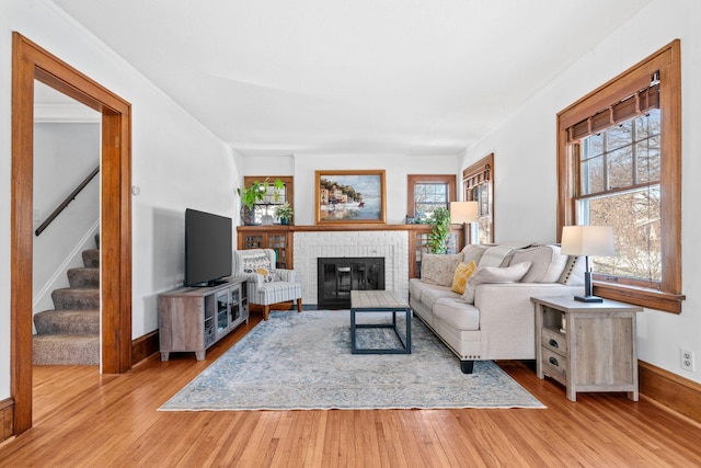 living room with stairs, a brick fireplace, a wealth of natural light, and light wood-style floors