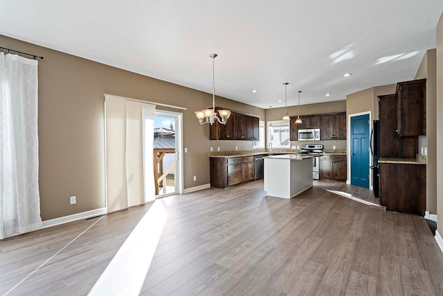 kitchen with light wood-type flooring, hanging light fixtures, a kitchen island, and appliances with stainless steel finishes