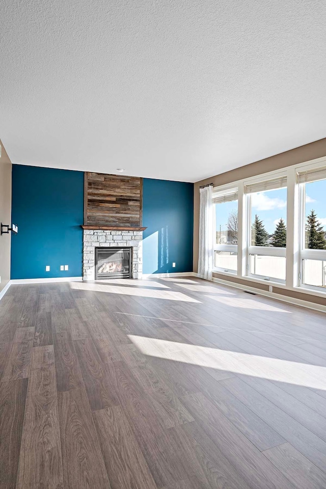 unfurnished living room featuring hardwood / wood-style flooring, a wealth of natural light, a fireplace, and a textured ceiling