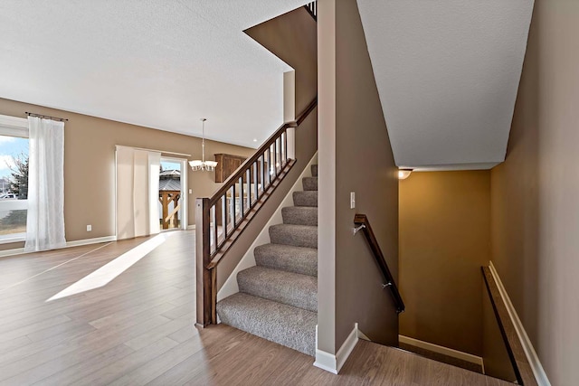 staircase featuring a textured ceiling, wood-type flooring, and a chandelier