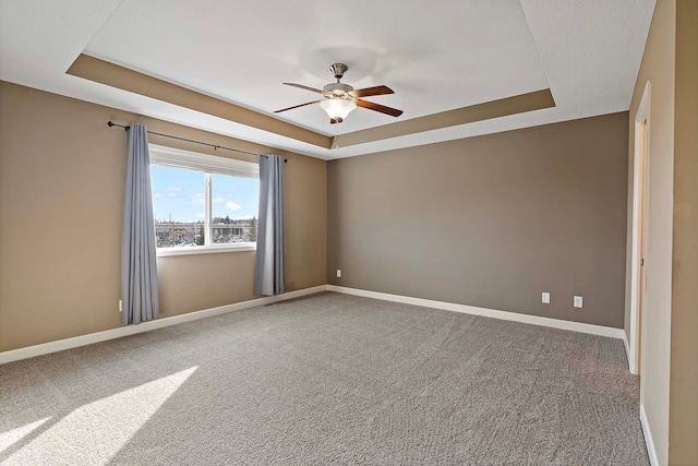 carpeted empty room with a raised ceiling and ceiling fan