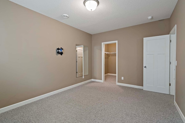 unfurnished bedroom featuring a spacious closet, light carpet, a textured ceiling, and a closet